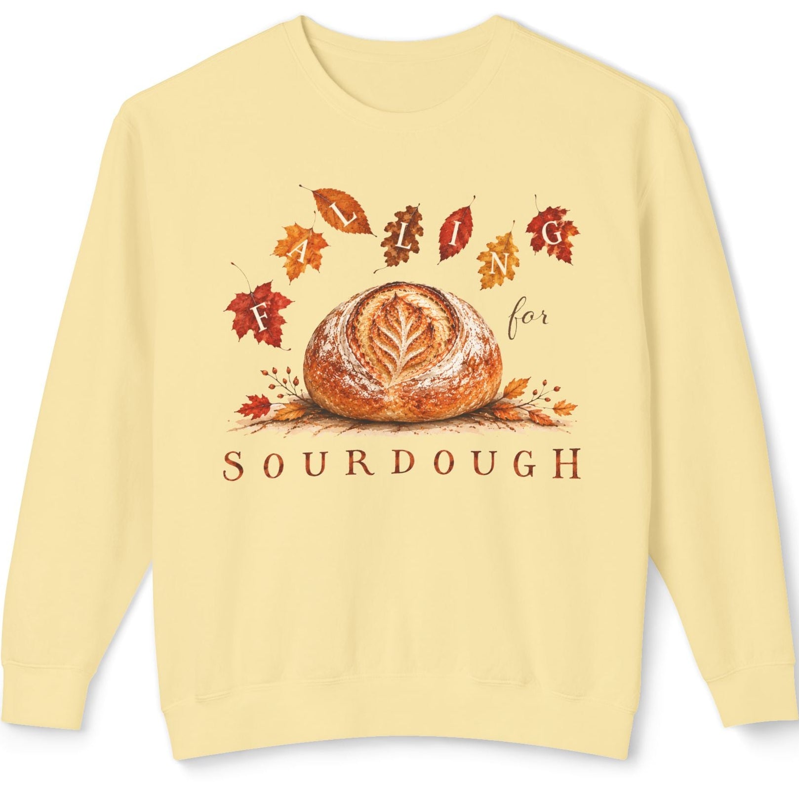 A pale yellow crewneck sweatshirt featuring a graphic print of a sourdough bread loaf surrounded by autumn leaves, with the word 'SOURDOUGH' printed below.