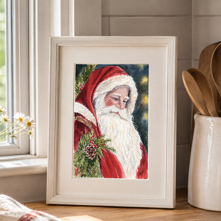 A framed art print of a painted Santa Claus holding a pine branch, styled on a wooden kitchen counter next to a vase of daisies and wooden utensils.